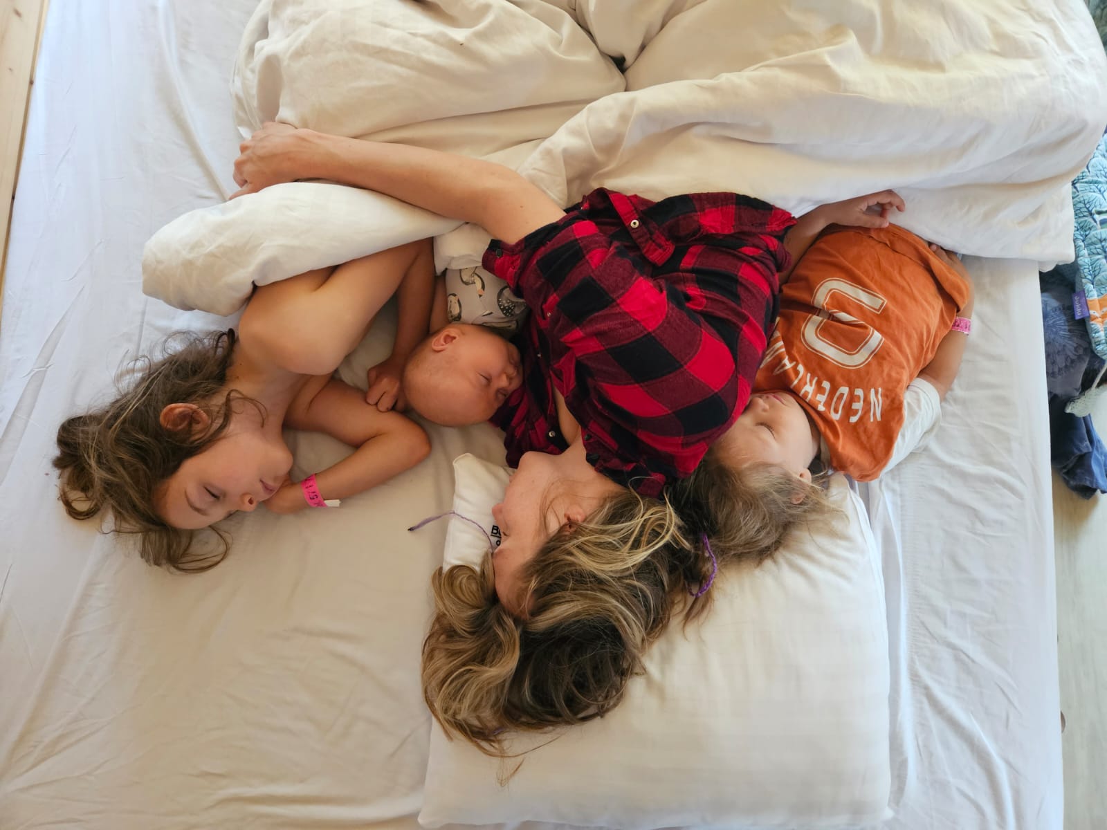 Mama śpi z trójką dzieci wtulonych w nią na łóżku
